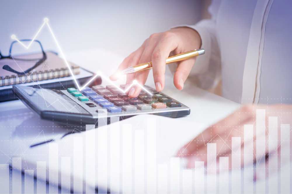 A person calculate tax while analyzing financial data, with graphs and charts overlaying the image.