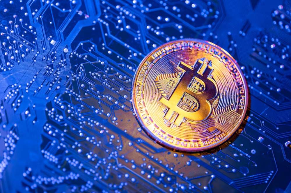 A close-up of a golden Bitcoin on a blue circuit board background, representing cryptocurrency and digital finance technology.
