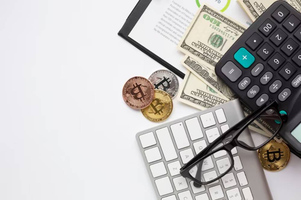 A calculator, glasses, a keyboard, cash, and Bitcoin coins on a desk, symbolizing finance and cryptocurrency management.