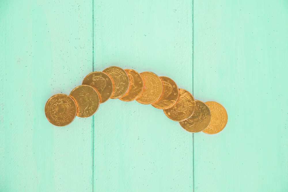 A row of shiny gold coins arranged in a curved line on a mint green wooden surface.