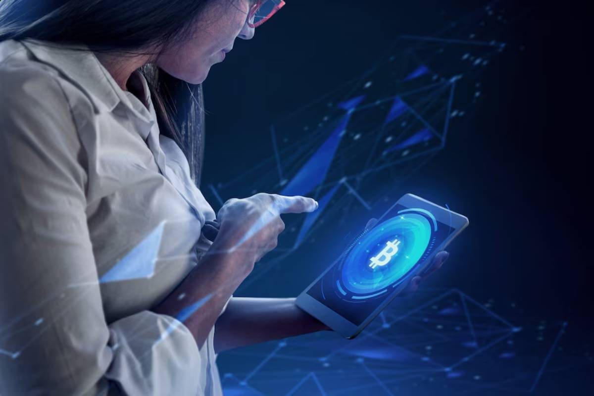 A woman with glasses points at a tablet displaying a glowing Bitcoin symbol, set against a dark, digital background.