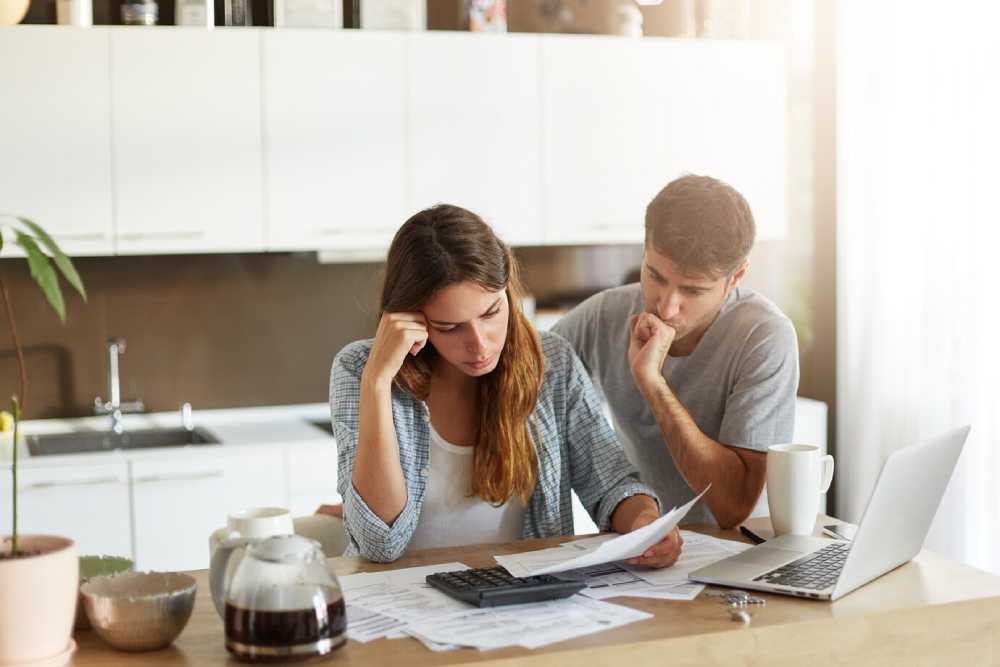 A couple examines papers and financial documents , surrounded by coffee and a laptop, appearing stressed.