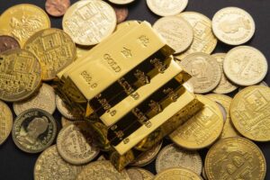 Three gold bars stacked on a pile of assorted gold coins, gleaming against a dark background, showcasing their luxurious value.