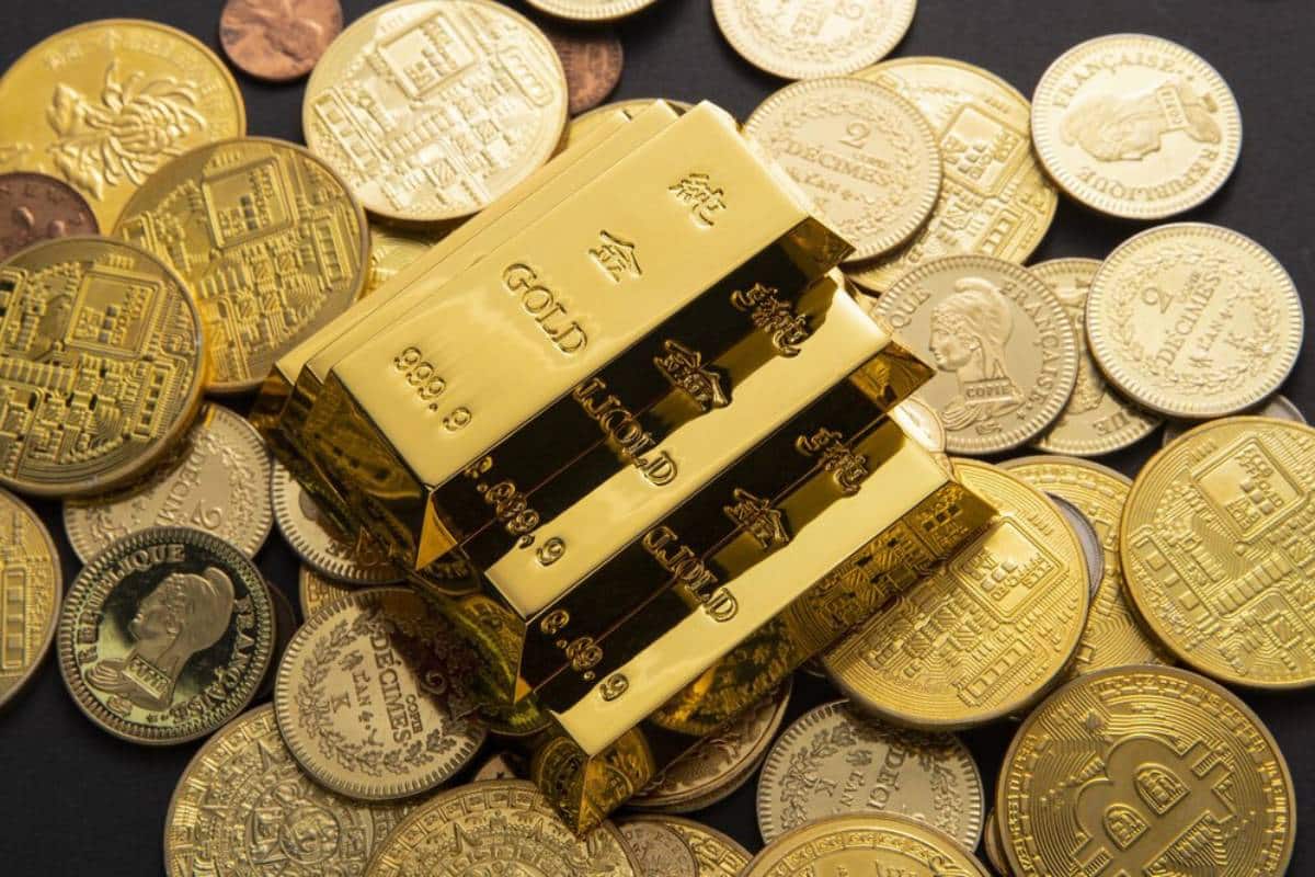 Three gold bars stacked on a pile of assorted gold coins, gleaming against a dark background, showcasing their luxurious value.
