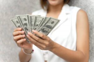 A woman in a white vest holds several hundred-dollar bills in her hands.