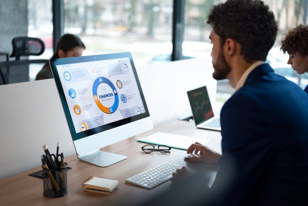A person in a suit sits at a desk, actively engaging with a computer displaying a financial infographic in a modern office setting.