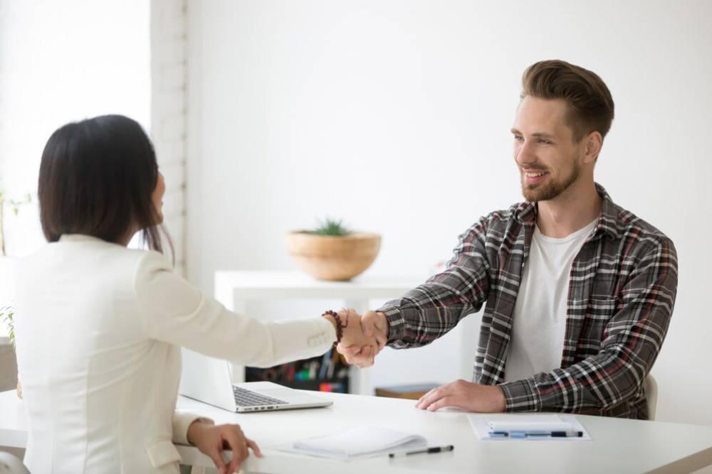 A professional setting where a woman in a blazer shakes hands with a man in a plaid shirt, signaling a positive interaction.