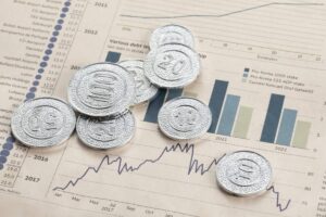 A collection of silver coins marked 10, 20, 50, and 100 resting on a financial report featuring graphs and data charts.