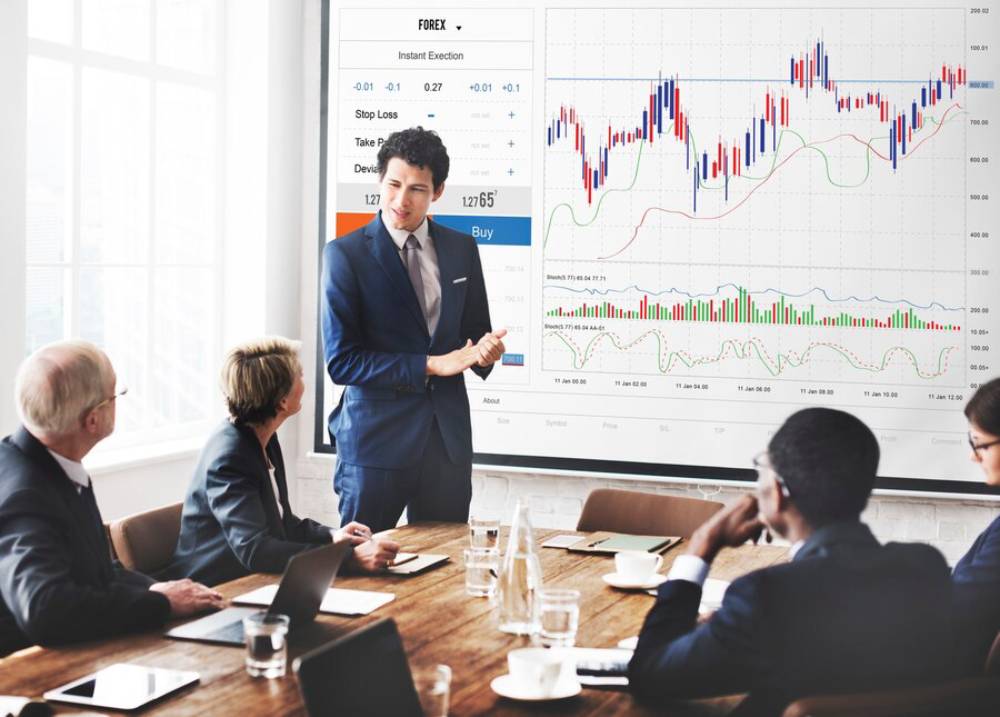 A businessman presents Forex trading data to a group of attentive colleagues in a modern conference room.