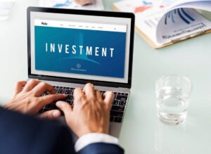 A person types on a laptop displaying an "Investment" webpage, with a glass of water nearby.