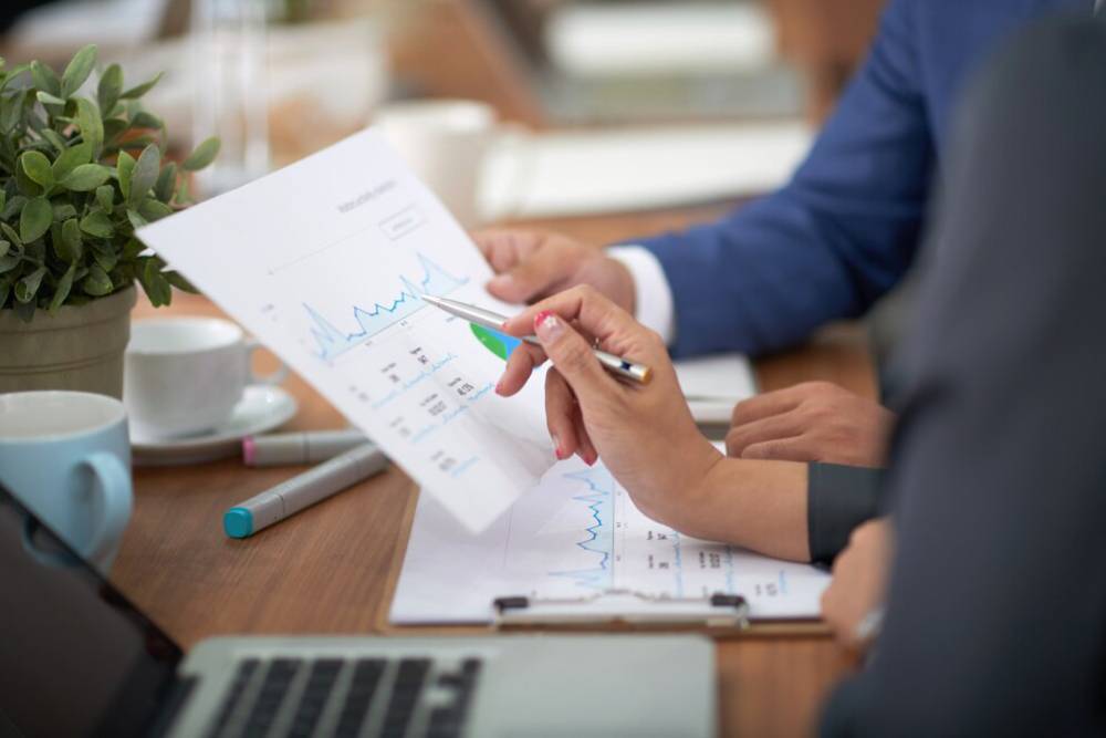 Two professionals analyzing business charts and graphs during a meeting, with a laptop and coffee cups in the background.