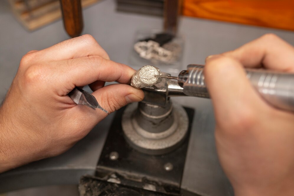 A jeweler uses a rotary tool to engrave intricate details on a silver pendant while securely holding it in a vice.
