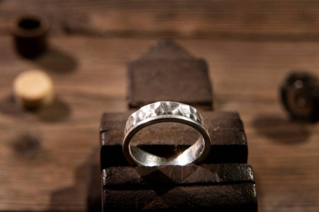 A hammered silver ring displayed on a rustic wooden workbench, with crafting tools softly blurred in the background.