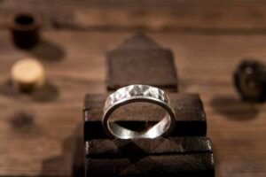 A hammered silver ring displayed on a rustic wooden workbench, with crafting tools softly blurred in the background.