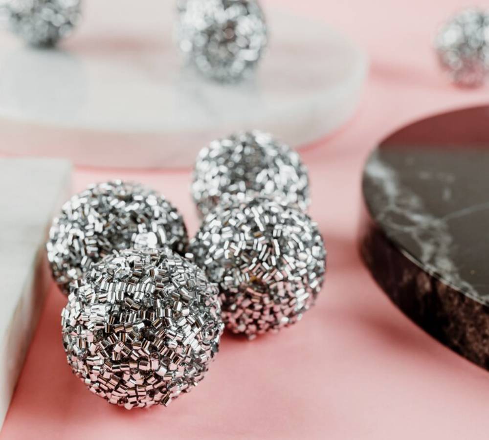 Silver metallic spheres made of small, shiny pieces scattered on a pink surface, alongside marble and slate platters.