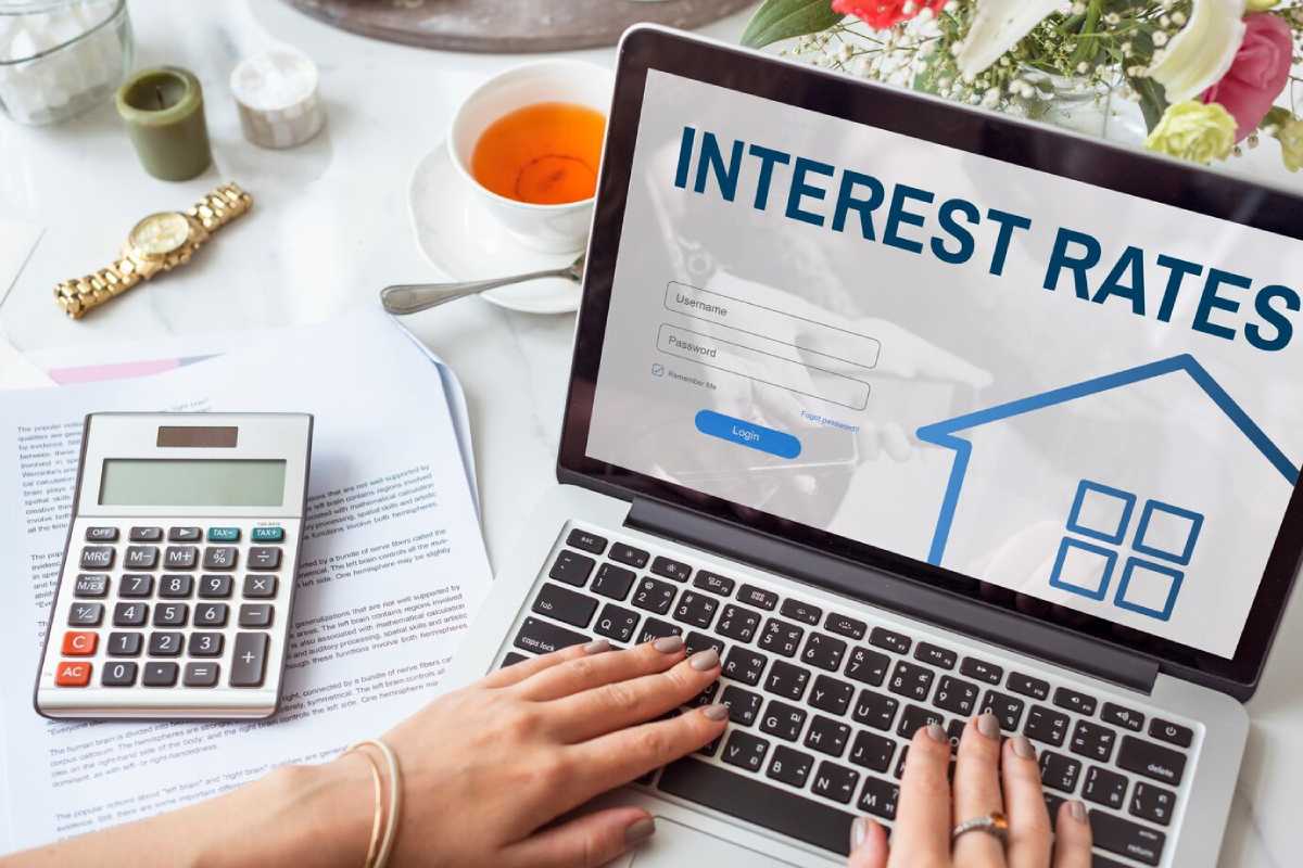 A person typing on a laptop displaying "Interest Rates" login page, with a calculator, documents on a table.