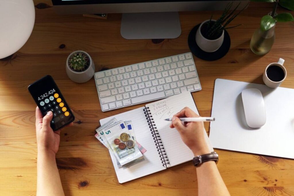 A top-down view of a desk with a calculator, money, a notebook, and a computer setup, showcasing financial planning or budgeting.