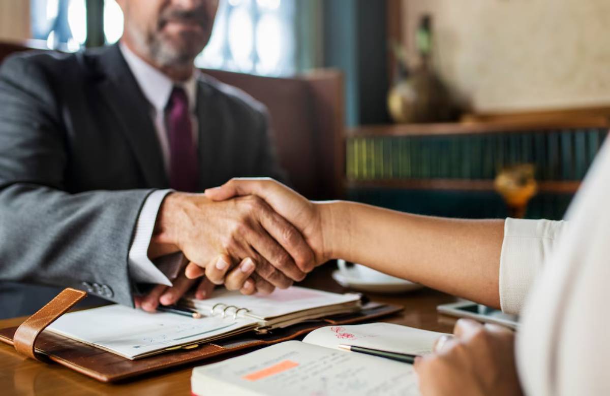 A businessman and a woman shake hands over a table with notebooks, symbolizing a professional agreement or partnership.